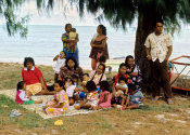 Wilcommen, No. 0164 A Local Family Sits on a Blanket on the Beach with their Children Enjoying Soft Drinks